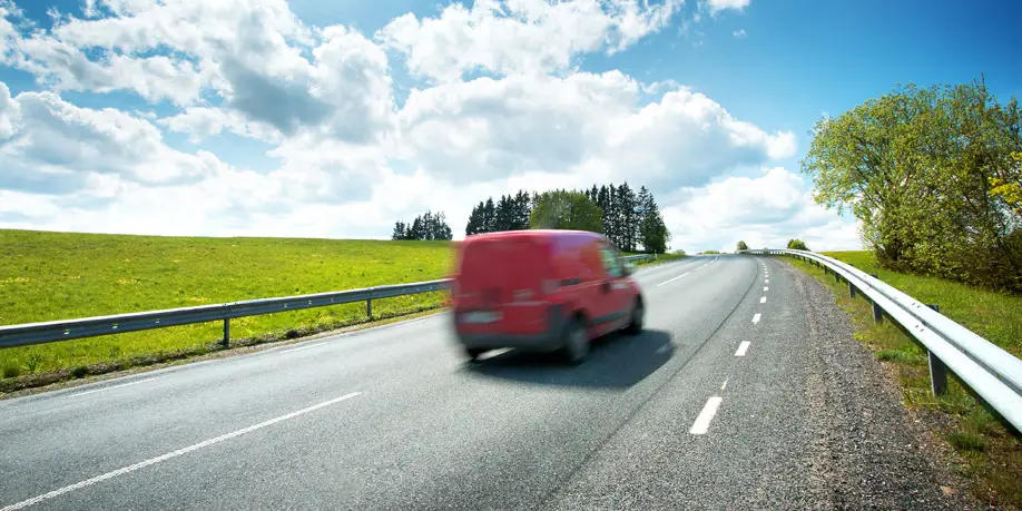 Red car driving along a sunny road