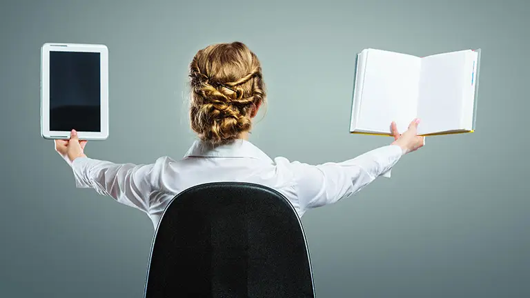 A woman comparing a digital screen and a printed page