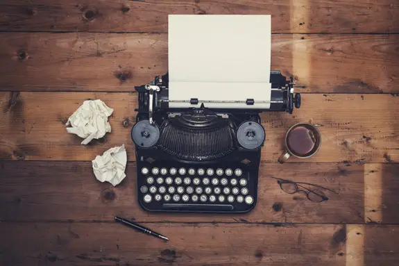 An old-fashioned typewriter next to a couple balls of crumpled up paper