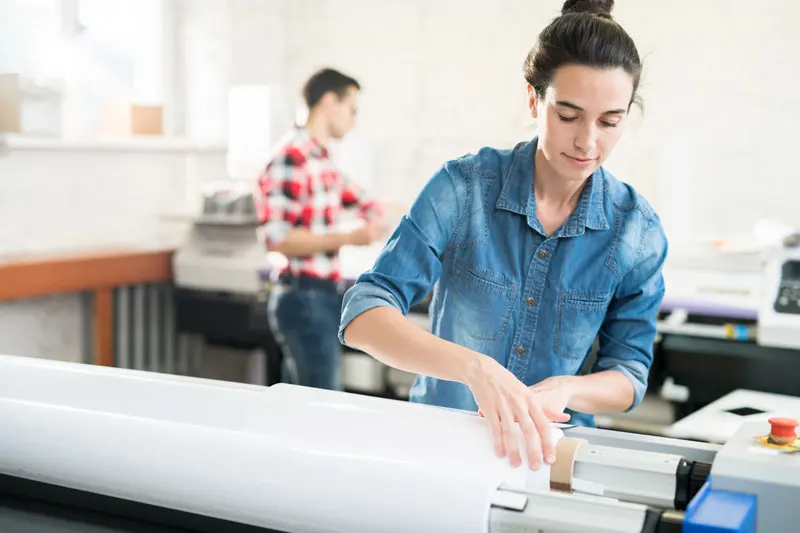 A woman installing a paper roll in a large format printer